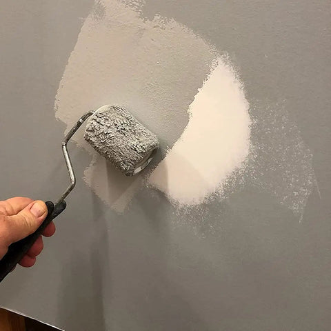Hand using a paint roller on a patched wall after using the Drywall Repair Kit With Tapered Hole Saw And Two Plugs For Clean Flat Patches.
