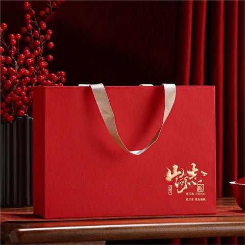 Red gift box with gold detailing and beige handle, displaying a decorative design, ideal for storing or presenting items.