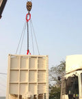 Front view of a Baluue chain sling with red hooks on both ends hoisting a large beige cargo container.