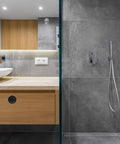 Modern bathroom with hidden handle embedded in wooden cabinets next to sleek gray tiled shower area.
