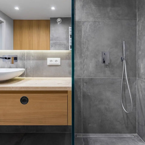 Modern bathroom with hidden handle embedded in wooden cabinets next to sleek gray tiled shower area.