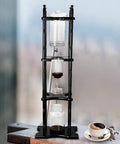 Big Batch Cold Brew Drip Coffee Maker With Roomy Glass Carafe And Solid Wood Base Built For Zero Friction Weekend Chill Vibes Pours Down Silky Smooth Low Acid Iced Coffee Perfect For Casual Hangouts Or Quick Office Grabs Yielding Twenty Rich Sips displayed on a wooden table with coffee cup.