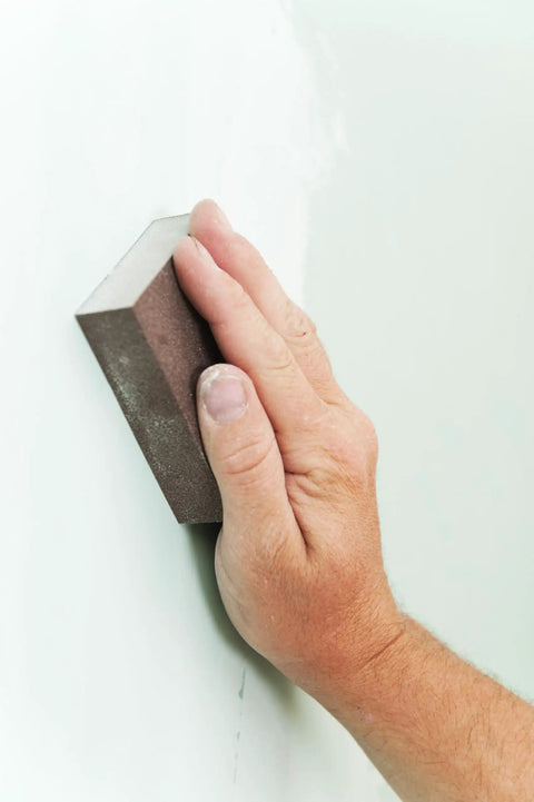 Hand using Six Pack Extra Fine Grit Sanding Sponges For Sanding Wood Paint Metal Plastic And Drywall Conforms To Surfaces