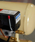 Brass 1/4'' NPT safety relief valve installed on an air compressor tank, with red pull cap on the valve stem.