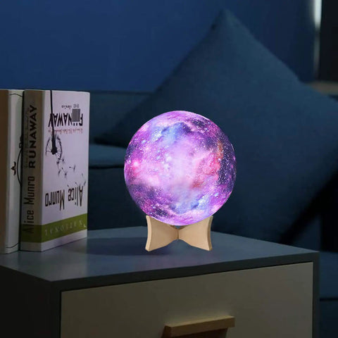 Colorful galaxy-themed night light on a wooden stand, emits purple and pink glow, beside books, on a bedside table.
