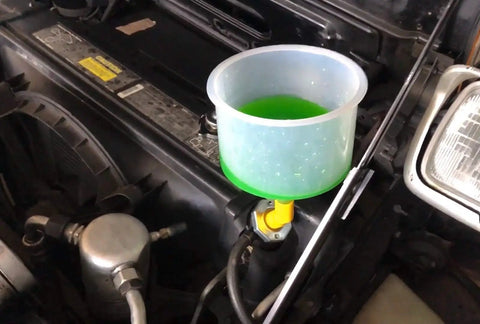 Universal Spill Proof Coolant Fill Funnel Kit With Complete Adapter Set For All Vehicles in use, featuring a transparent funnel and coolant.