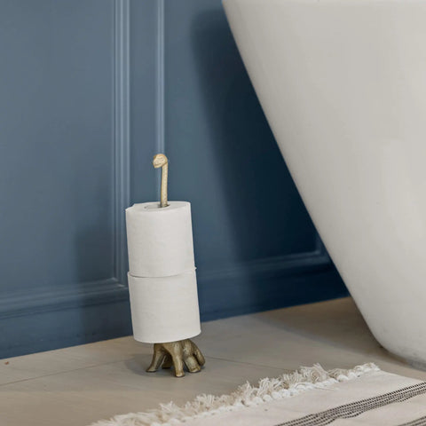 Totally Gold Dino Paper Towel Holder Stand for Kitchen and Bathroom Decor next to a bathtub, holding rolls of paper.