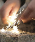 Person using waterproof magnesium firestarter kit 2 in 1 with flint serrated striker on a rock, creating sparks for camping