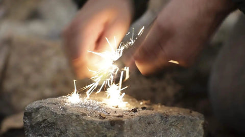 Person using waterproof magnesium firestarter kit 2 in 1 with flint serrated striker on a rock, creating sparks for camping