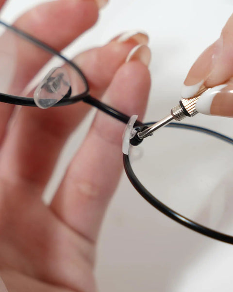 Hand holding eyeglasses while using tool to adjust nose pad, showcasing Complete Eyeglass Repair Kit With 1000 PCS In 32 Slot Blue Case Featuring Rust Proof Stainless Screws Soft Silicone Nose Pads Tweezers And Cloths For Quick No Sweat Fixes To Frames And Shades On The Go.