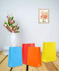 Four colorful party favor bags on a table, part of the 32 Pack Kraft Paper Gift Bags With Handles Six Color Rainbow Set for parties.