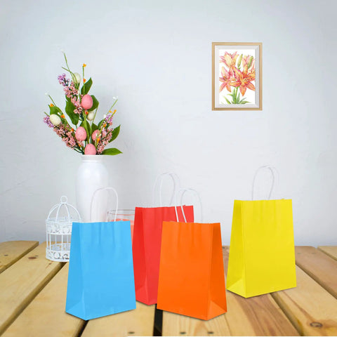 Four colorful party favor bags on a table, part of the 32 Pack Kraft Paper Gift Bags With Handles Six Color Rainbow Set for parties.