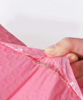 Close-up of a hand peeling self adhesive seal on 60 Pack Pink Bubble Mailers 12x18 Plus 4 Inch Self Adhesive Padded Envelopes