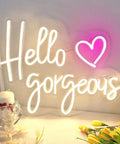 Hello Gorgeous Neon Sign For Girls Bedroom Wall Decor LED Light With Warm White Glow Perfect For Birthday Parties Weddings And Gifts 16.7x12.3 Inches Great Gift Idea displayed on a desk with decorative flowers