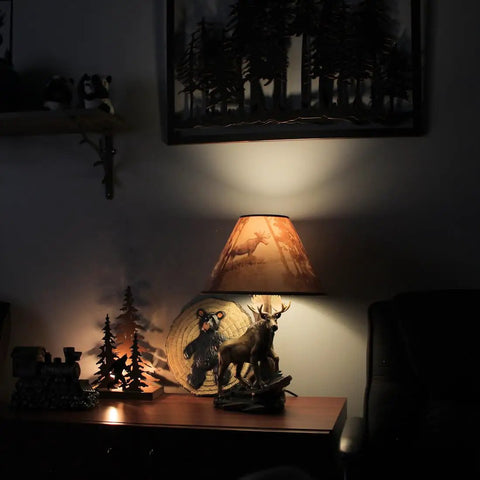 Wildlife Moose Table Lamp With A 12 Inch Forest Print Lampshade For Living Rooms Cabins And Bedrooms Delivers Cozy Warm Glow And Striking Rustic Decor Standing 20 Inches Tall For A Commanding Home Accent in a dimly lit room.