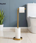 Gold freestanding toilet paper holder stand with reserve for four rolls, sturdy base, next to a white toilet and potted plant.