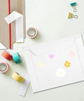 100 Pcs 6.5 By 4.5 Inch Rigid Mailers With Self Seal Envelopes Stay Flat Cardboard Mailers For Shipping Postcards Calendars Photos CDs Documents Comic Books And More; mailer on a surface with decorative tapes and clips
