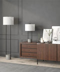 65.5 Inch Tall Floor Lamp With White Drum Shade In Blackened Bronze And Concrete Finish next to modern console, creating ambient glow.