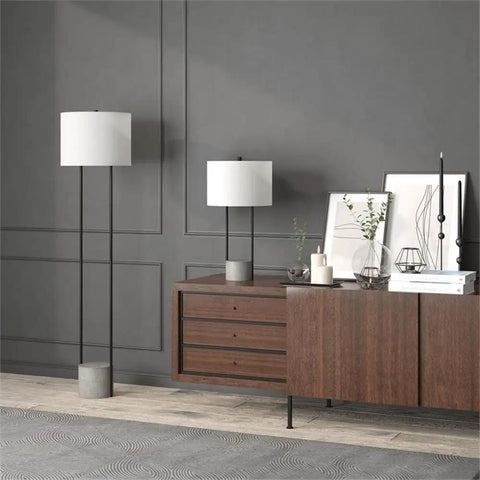 65.5 Inch Tall Floor Lamp With White Drum Shade In Blackened Bronze And Concrete Finish next to modern console, creating ambient glow.