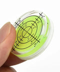 Close-up of a hand holding a 32mm round spirit level bubble with a green liquid indicator for precise leveling.
