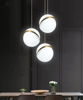 Three Acrylic Globe Pendant Lights With Irregular Hanging Design For Dining Room And Living Room Adjustable Cable 110 To 140 Volt UL Certified Includes Gold Ceiling Mount And Hardware For A Sleek Modern Vibe, with three globes hanging over a dining table.