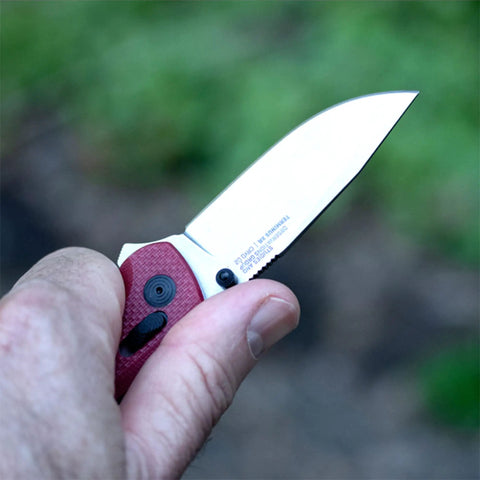 Close-up of a hand holding the Terminus XR G10 Folding Knife With Ambidextrous Opening, visible blade, crimson handle, outdoors.
