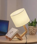 Cute Desk Lamp With Wood Base And Changeable Shape, ivory linen lampshade, on table beside plant and laptop, cozy vibe