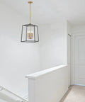 Dope Two Tone Farmhouse 4 Light Pendant Chandelier in black and warm brass hanging in a white hallway with geometric metal cage design.