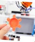 Hand holding orange plum-shaped rubber coupling pad for jaw couplings, pro-grade flexible shock absorbing cushion that reduces vibration