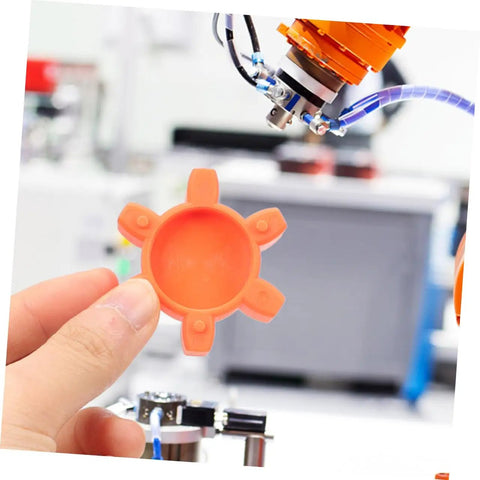 Hand holding orange plum-shaped rubber coupling pad for jaw couplings, pro-grade flexible shock absorbing cushion that reduces vibration
