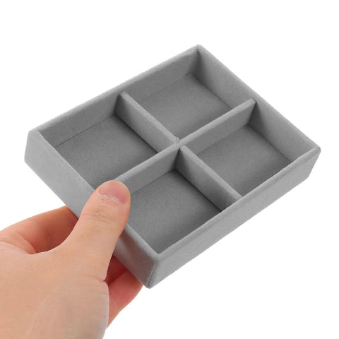 Hand holding a compact gray velvet jewelry organizer tray with four grid compartments, perfect for rings and bracelets.