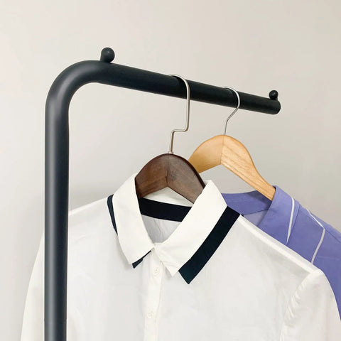 Close-up of Matte Black Metal Coat Rack Dope Modern Clothing Tree With Heavy Slate Base holding shirts on hangers