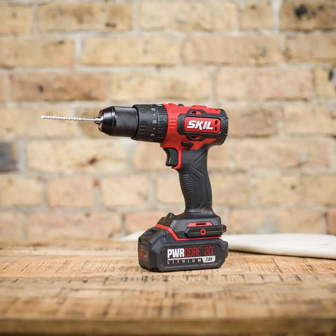 PWR CORE 20 Brushless 20V Cordless Hammer Drill Kit on table, showing drill bit and compact design against brick wall background.