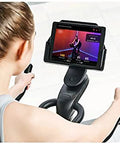 Person using Quiet Indoor Cycling Bike For Home Gym With Magnetic Resistance And Belt Drive Stable Steel Frame Adjustable Cage Pedals Smooth Low Impact Cardio Workout No Fuss Easy To Use And Store viewing virtual trainer on tablet