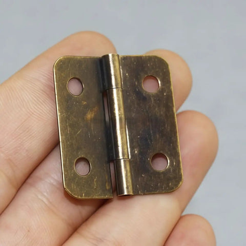 Person holding a 42 Piece Mini Hinge Set in Antique Bronze Finish, heavy duty cast iron, rounded corners, 30x27mm.