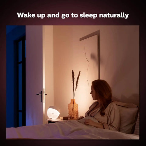 Woman in bed with gold smart table lamp with white and color ambiance LED that changes color, lit indirect lighting for bedroom