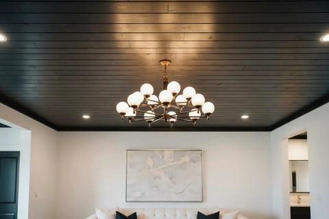 Modern interior featuring black wood ceiling and brass chandelier with white globes, creating a rustic industrial vibe.