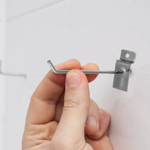 Close-up of hand installing Slatwall Hooks For Phone Accessories, Heavy Duty 50 Pack Iron Pegboard Display Hangers, Easy Setup No Tools Required