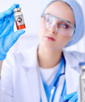 Sealed sterile 10 ml vial with red liquid held by gloved hand.