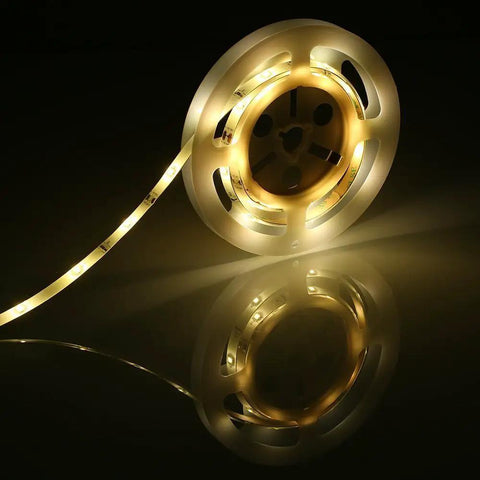 Motion Activated Bed Light With Flexible LED Strip on a reel, glowing warm soft light for bedroom nighttime navigation.