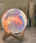 Galaxy Moon Lamp 4.8 Inch With Wood Stand, 16 Color Changing LED Moon Light glowing on desk with USB charging cable