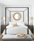 Minimalist bedroom with canopy bed, white bedding, wicker mirror, and two modern lamps on wooden nightstands.