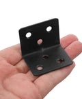 Hand holding a heavy duty L shaped corner bracket with screws, part of a 12 piece set made of cold rolled steel for DIY furniture projects.