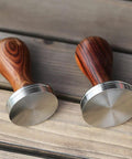 Two 51mm espresso tampers with wooden handles and stainless steel bases for stable tamping on wood surface.