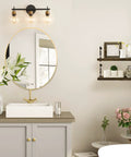Three Light Black And Gold Bathroom Vanity Light Fixture With Metal Base And Clear Glass Globe Shades, Modern Over Mirror Bath Lighting That Elevates Your Space With Sleek Durable Build And High End Look installed above round mirror in bathroom setting.