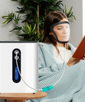 Woman using Hydrogen Face Mask H2 Inhalation Device With Full Face Shield relaxing in living room, reading a book.