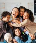 Smiling teacher with students holding 'Fun Geography And History Game With 225 Country Names And Capitals Flash Cards' in classroom