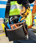 Tradesman Pro Tool Pouch With Padded Shoulder Strap And Reinforced Bottoms 15 Pocket Tool Organizer worn by worker on ladder.