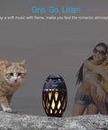 LED Flame Outdoor Table Lamp With Bluetooth Speaker Rechargeable Ambience Lantern beside a cat and couple outdoors.