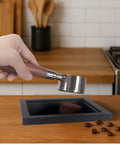 Hand holding portafilter over Stainless Steel Coffee Grounds Box for Espresso Machines, Black Bar Trash Bin With Rubber Bottomless Design